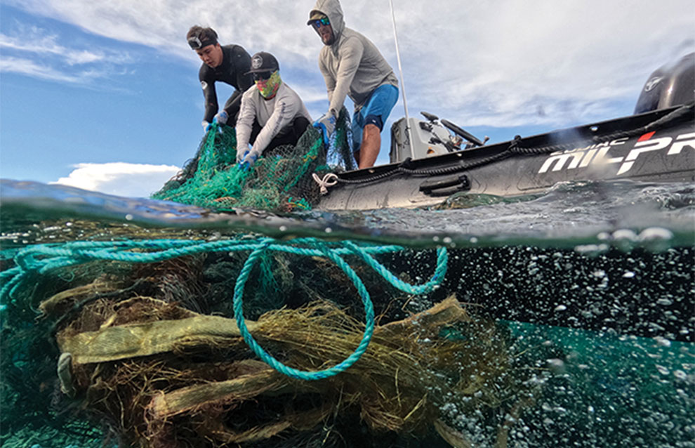 view half shot underwater of three people pulling up a blue net into their black raft.
